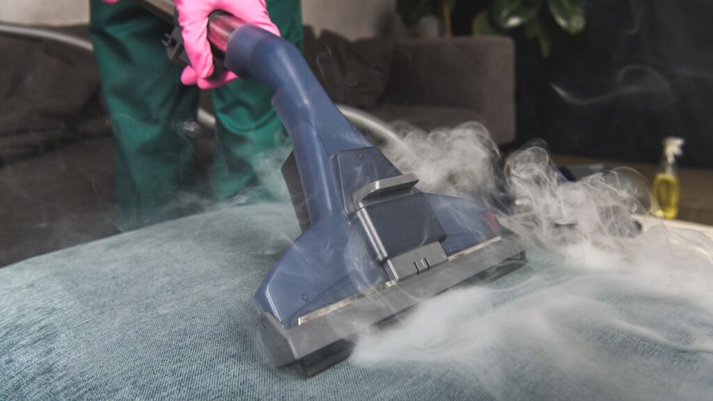 Steam cleaner head releasing vapor while sanitizing fabric sofa.