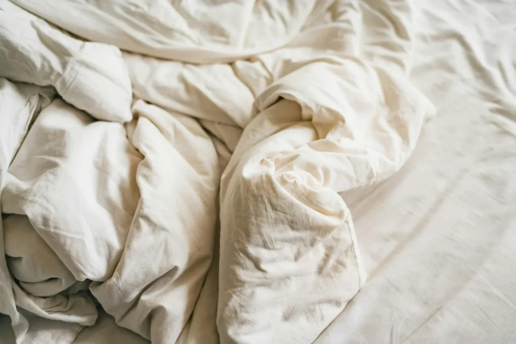 Zgužvani bijeli poplun na krevetu – neuredna posteljina nakon spavanja