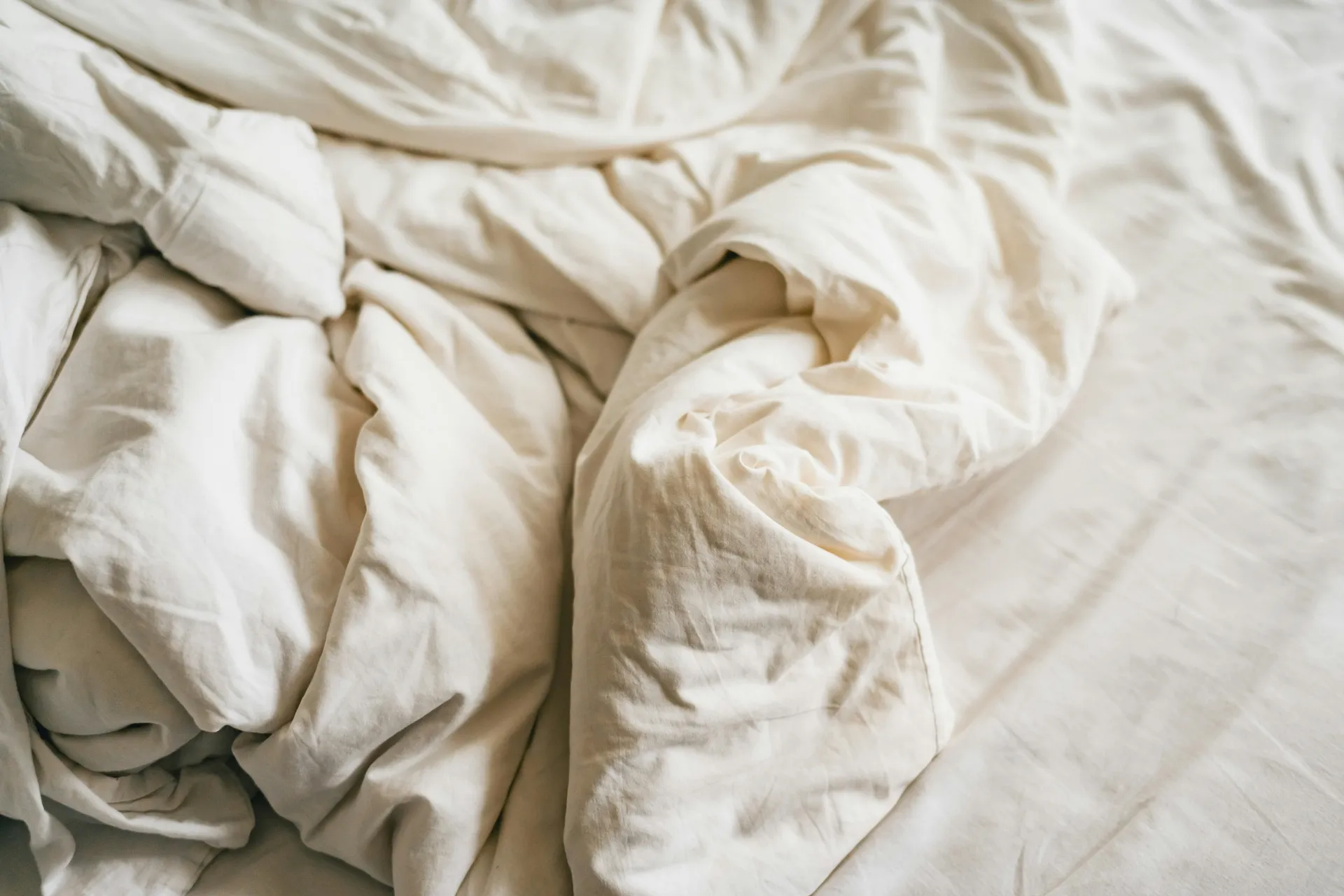 Zgužvani bijeli poplun na krevetu – neuredna posteljina nakon spavanja